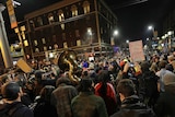 Hundreds of people with their backs to the camera, holding signs, a horn in shot