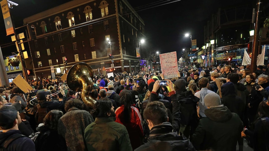 Hundreds of people with their backs to the camera, holding signs, a horn in shot