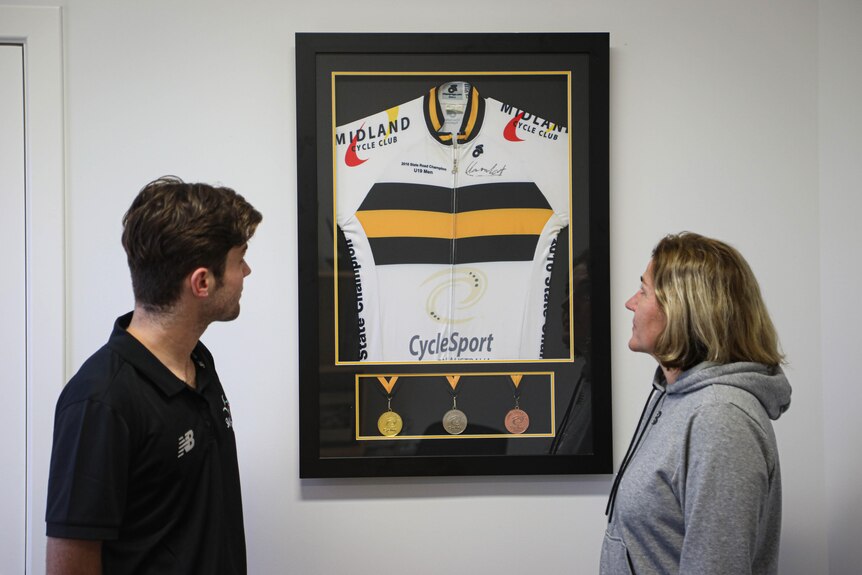 A man and woman look at a framed sports jersey hanging on a wall.