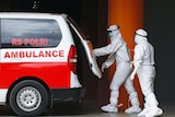 Two healthcare workers in white PPE close the boot of an ambulance