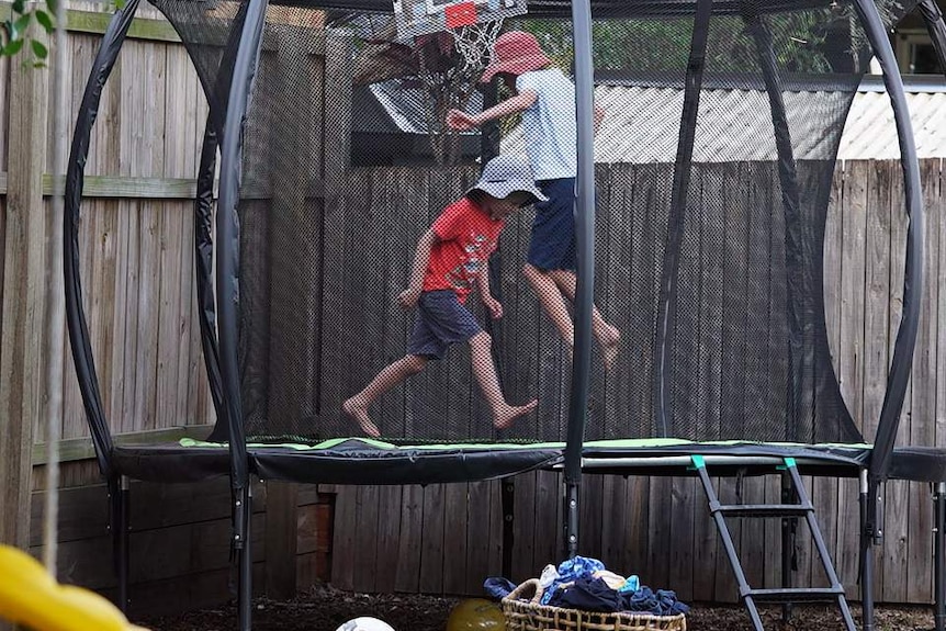 Two anonymous primary school-aged boys play on a trampoline in a backyard of a house in Australia.