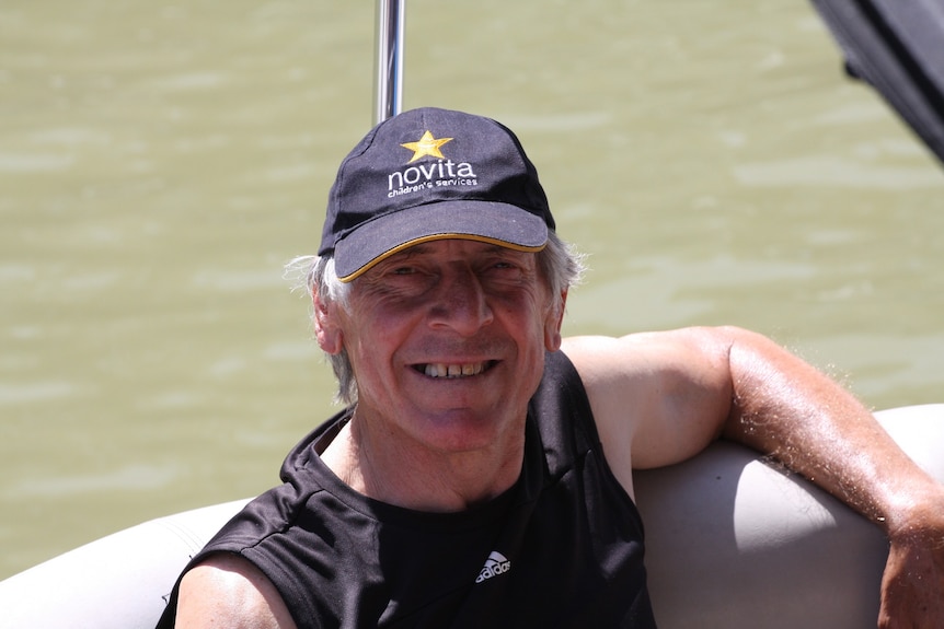 Russell Ebert wears a hat and smiles at the camera inside a boat. His hat is blue. He wears a grey shirt.