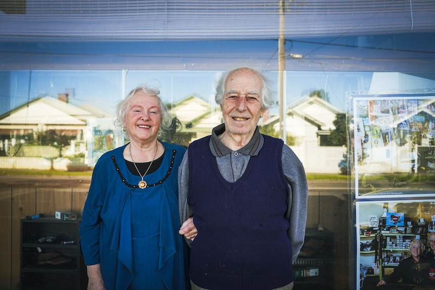 Nerina stands holding Peter outside their shop, with neighbouring homes seen in the glass