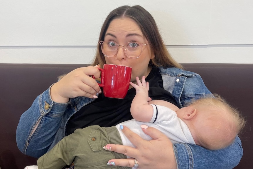 woman drinking from a mug while breastfeeding a baby