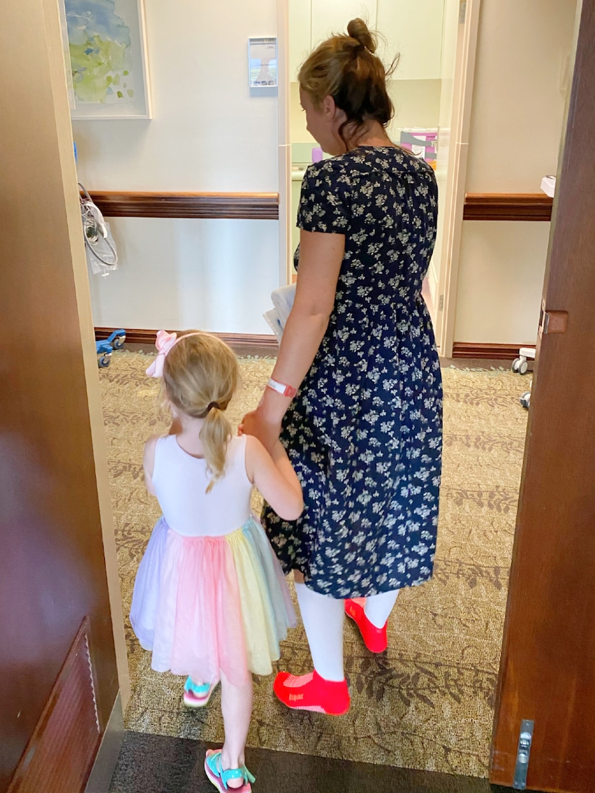 Woman wearing support socks holds a child's hand as they walk out of a hospital room.