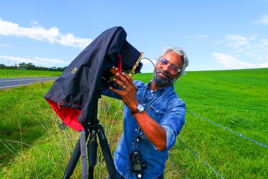 A man holds his film camera standing by the side of the road. 