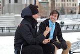 Two young men sit on park bench in conversation