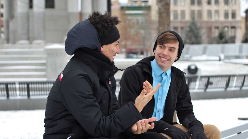 Two young men sit on park bench in conversation