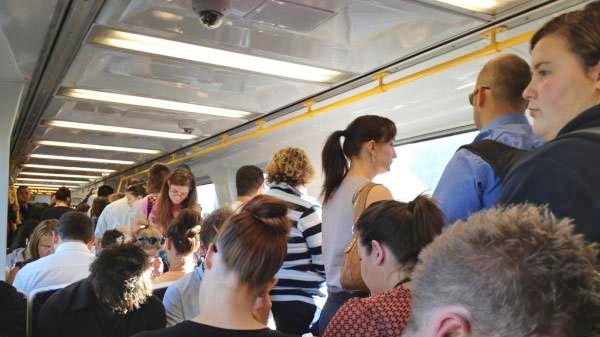 People sitting and standing inside a train carriage.