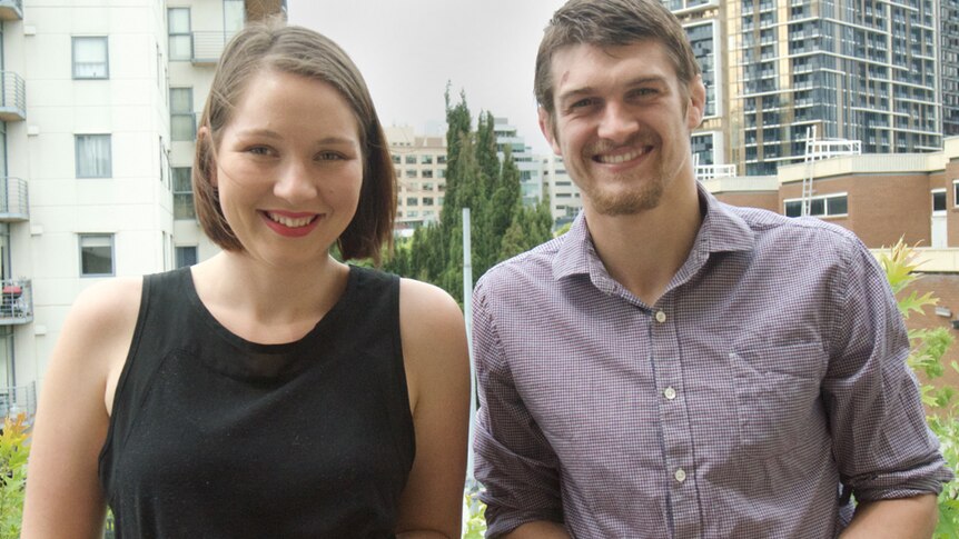 Two young people, aged in their twenties, smiling in front of high-rise apartment buildings