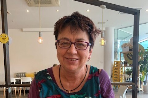 Photograph of a white woman with short dark hair and glasses, sitting in a cafe