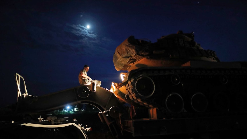 Under moonlight, Turkish army officer uploads a tank from a truck to its new position on the border between Turkey and Syria