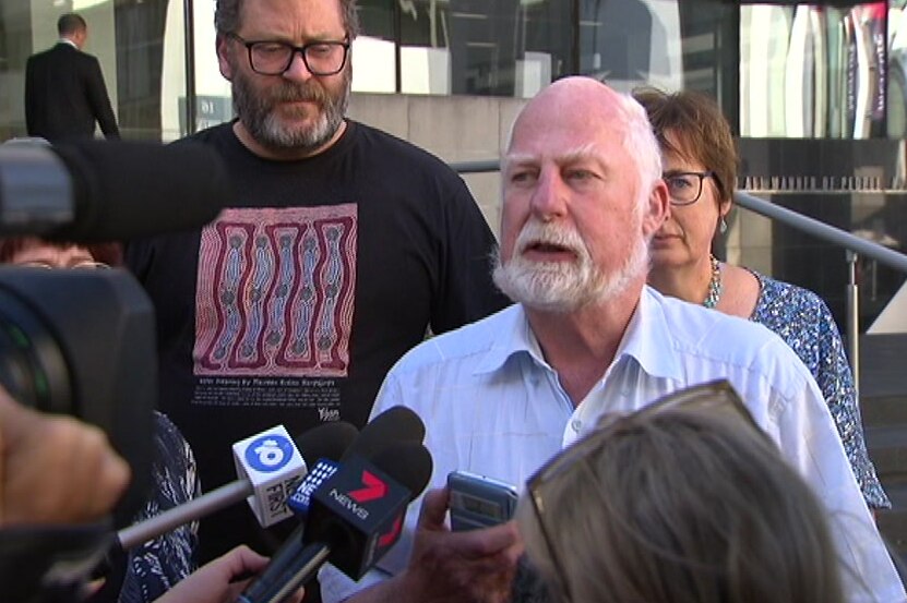 Anton Rogers speaks to reporters outside a Perth court with a man and a woman standing behind him and microphones in front.