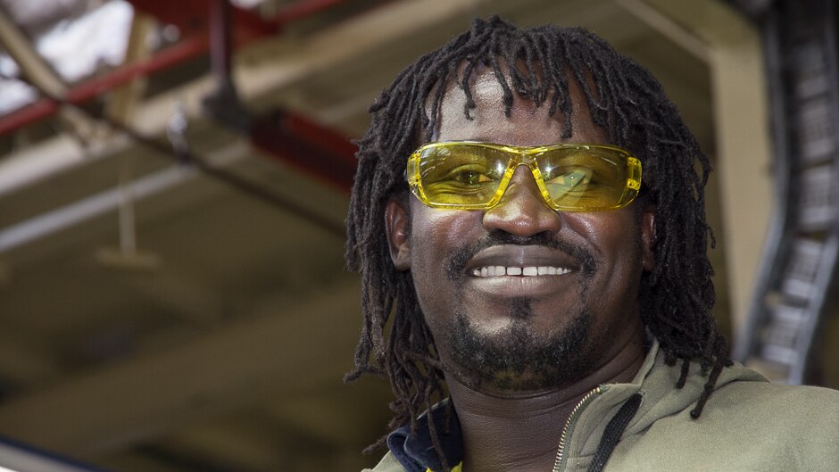 A man in factory yellow glasses with a blurred background of a factory