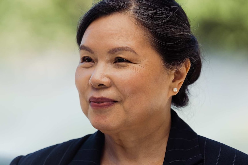 A headshot of a woman in a suit in front of some trees.