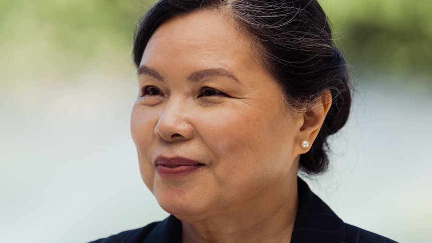 A headshot of a woman in a suit in front of some trees.