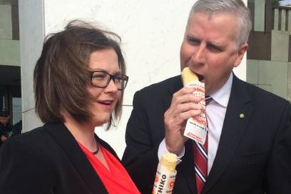 A man and a woman in suits eat Chiko Rolls.