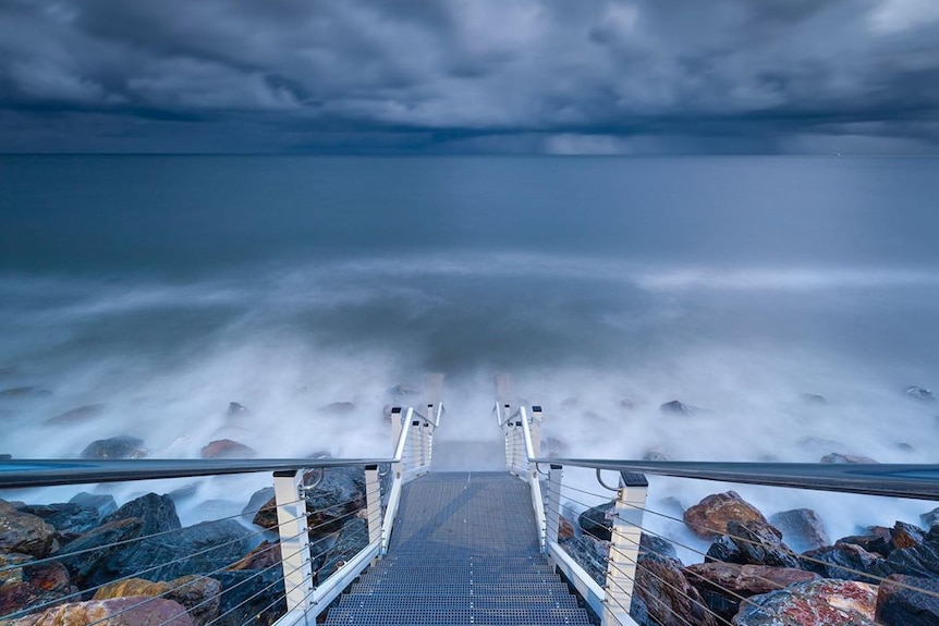 A storm arrives over West Beach, with stairs to the shore in the foreground.
