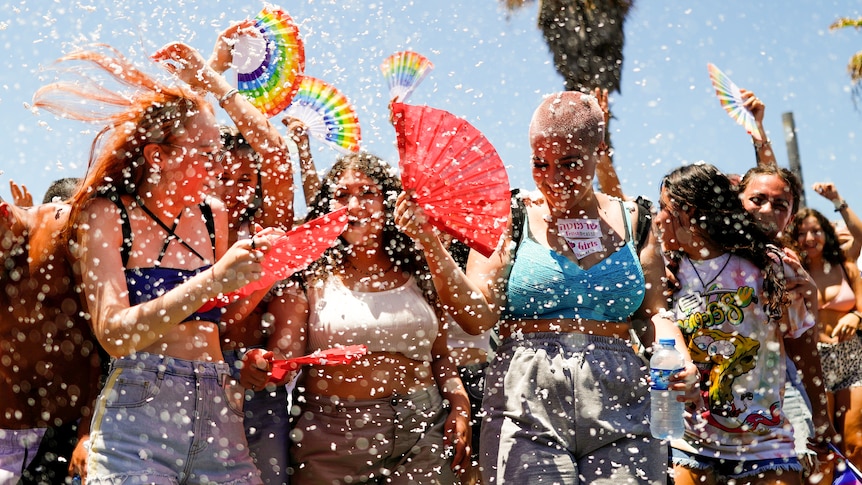 A group of young women with fans laughing as water droplets spray through the air 