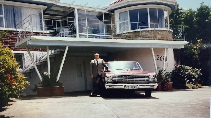 Photograph of a man standing in front of a house