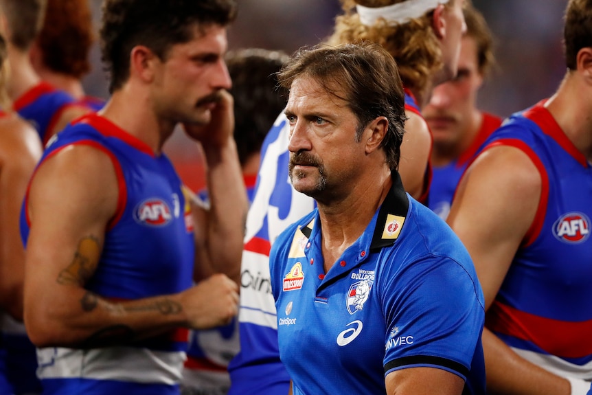 A man in a blue and red polo with a handle bar moustache