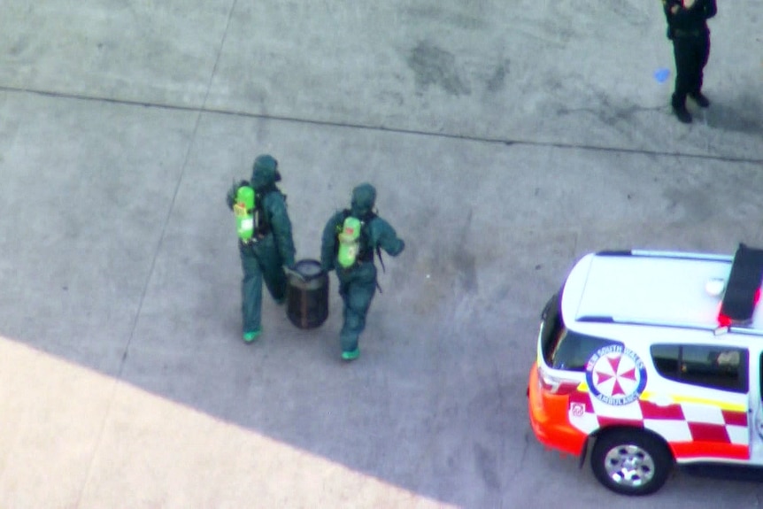 two men dressed in hazmat clothing carry a canister 