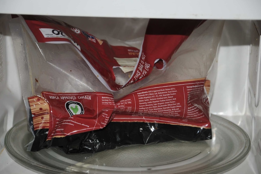 The remains of a barbecue chicken in its original bag sit inside an open microwave