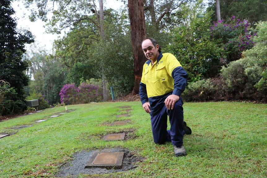 Cemetery worker Michael McMaster kneeling inspecting theft of copper plaques 