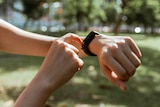 Person pointing at fitness tracker on wrist with greenery in the background