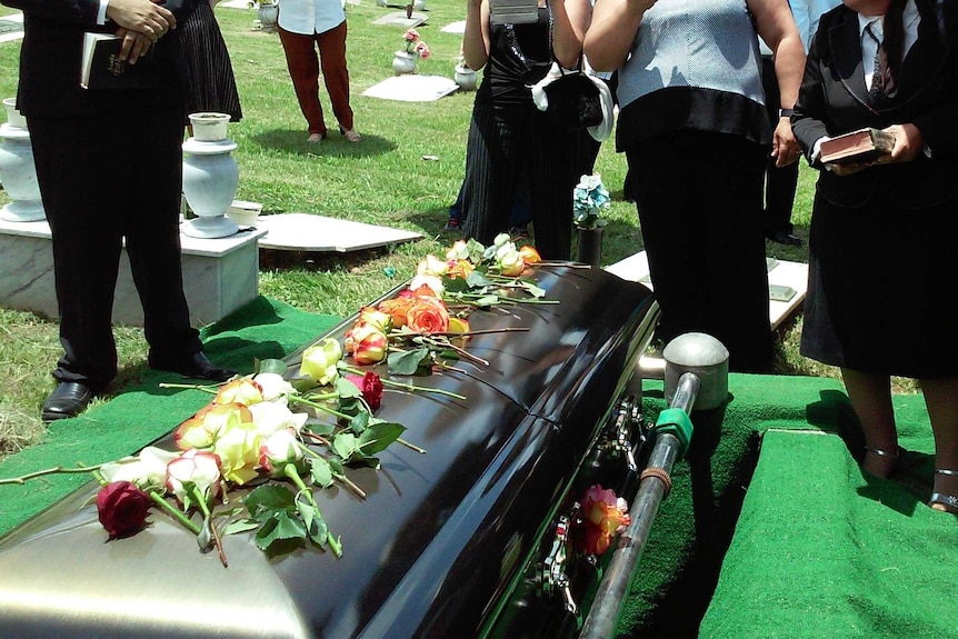 A coffin about to go into a grave with people standing around it
