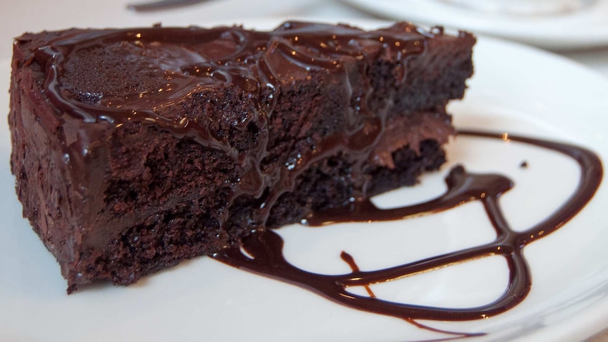 A slice of chocolate cake, drizzled with chocolate sauce, on a white plate.