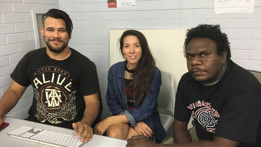 The three sit sit behind a desk, in front of a grey wall