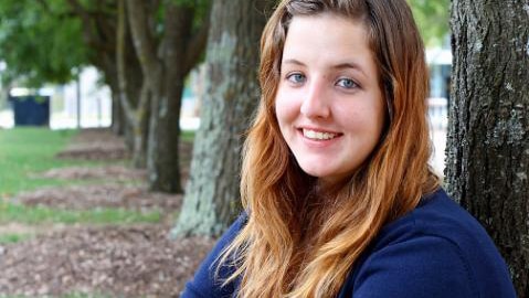 Teenage girl sits against tree