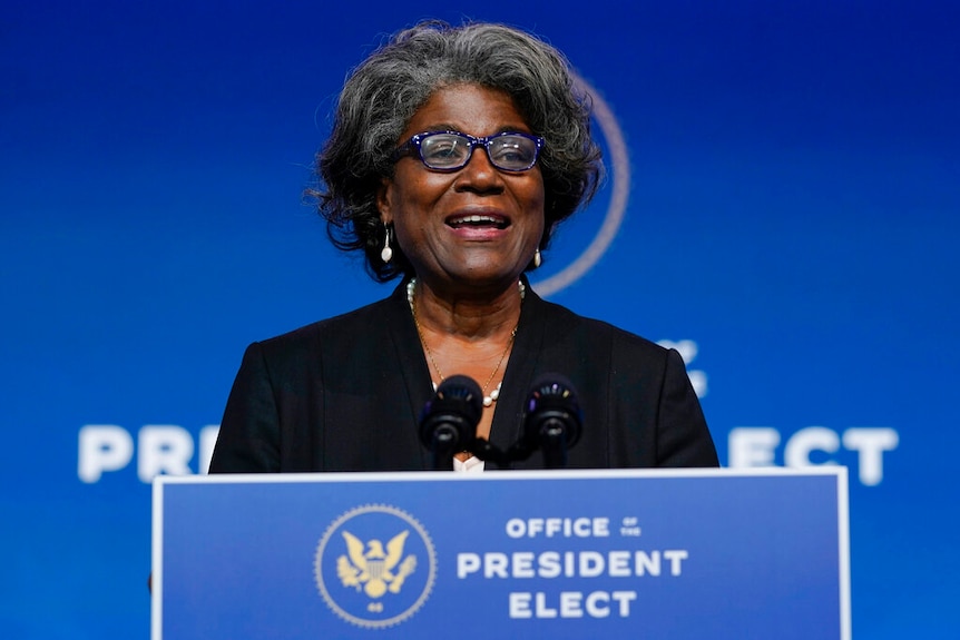 You view a woman of African-American descent with greying hair stand behind a dark blue lectern of the US President-elect.