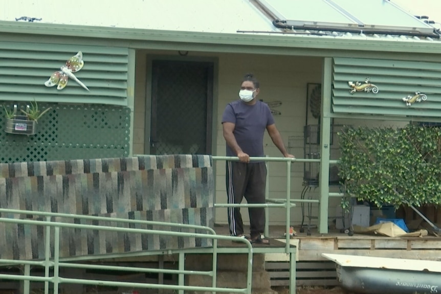 A man wearing a mask stands on the ramp to his front porch.