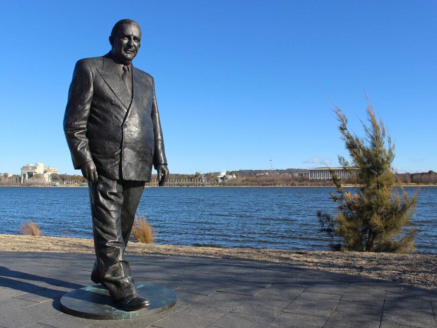 A bronze statue of a man in front of Lake Burley Griffin.