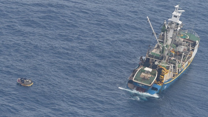 Aerial shot of fishing boat sitting along side small dinghy in the ocean.