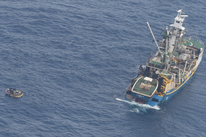 Aerial shot of fishing boat sitting along side small dinghy in the ocean.