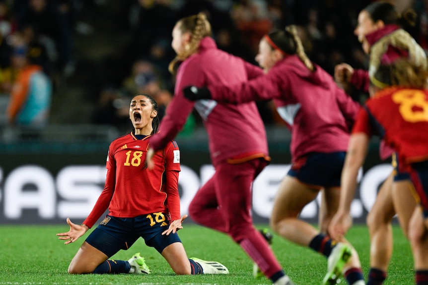 Salma Paralluelo screams on her knees as Spain teammates run onto the field after a Women's World Cup win.