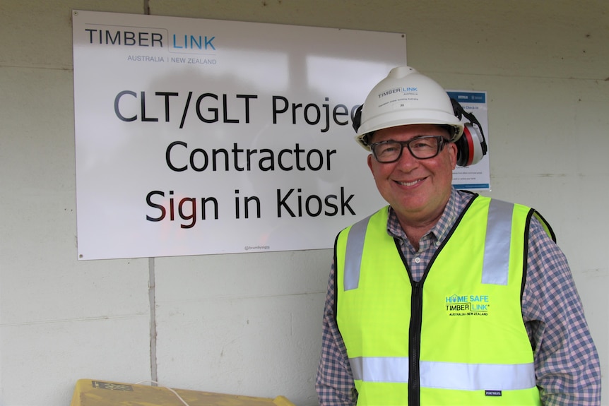A man in a high-vis vest and hard hat smiles at the camera with a sign reading 'CLT/GLT project contractor sign in'