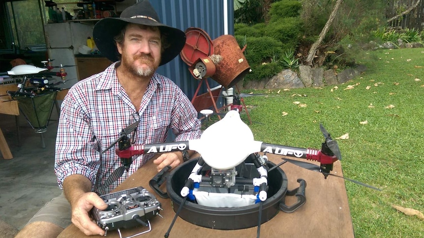 Ash Smith sits at a table with a six-propeller drone fitted with a hopper designed to distribute ant baits.