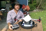Ash Smith sits at a table with a six-propeller drone fitted with a hopper designed to distribute ant baits.