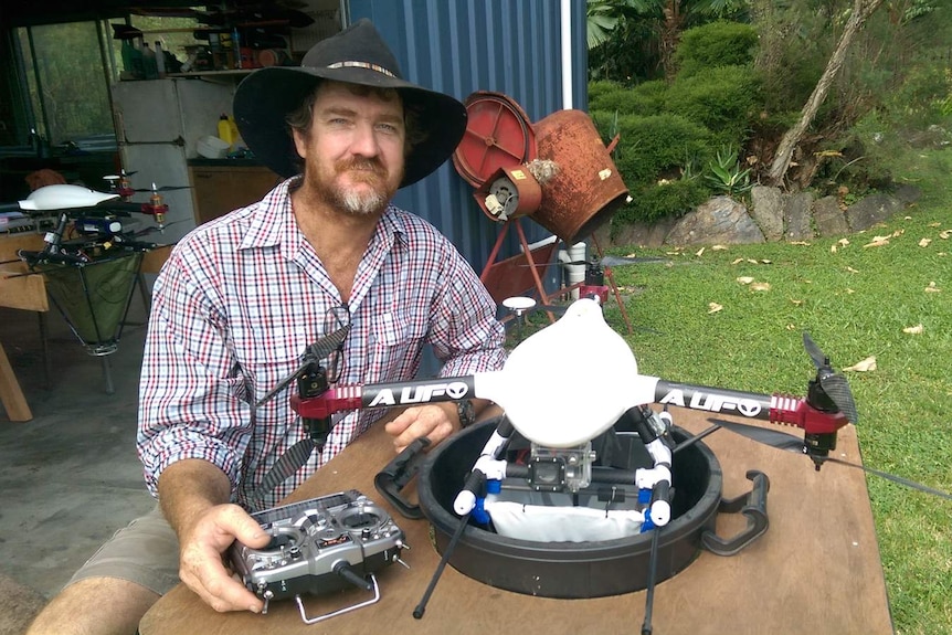 Ash Smith sits at a table with a six-propeller drone fitted with a hopper designed to distribute ant baits.