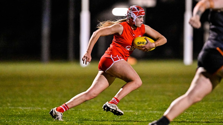 A woman in red and white headgear runs with a ball under her arm