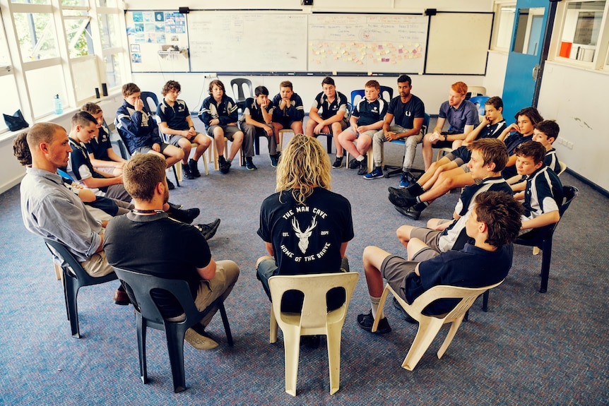 Group of young men and teenage boys sit in a circle in a classroom