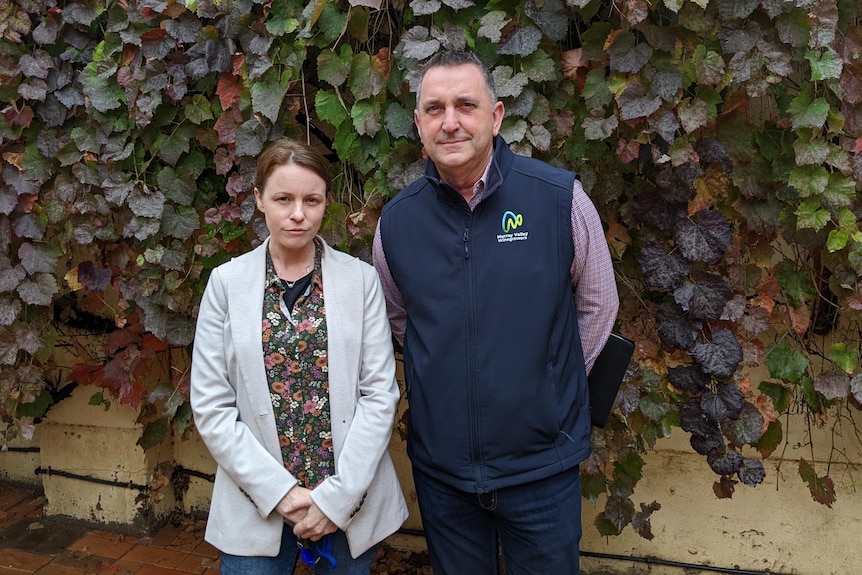 A woman and man stand in front of a wall covered in leaves