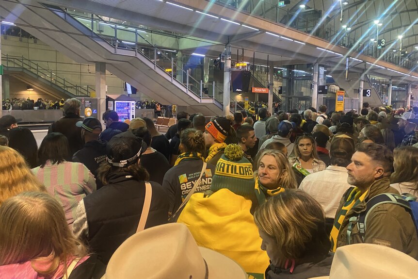 Eine Nahaufnahme einer Menge Fans in Matildas-Farben, die am Bahnhof warten 