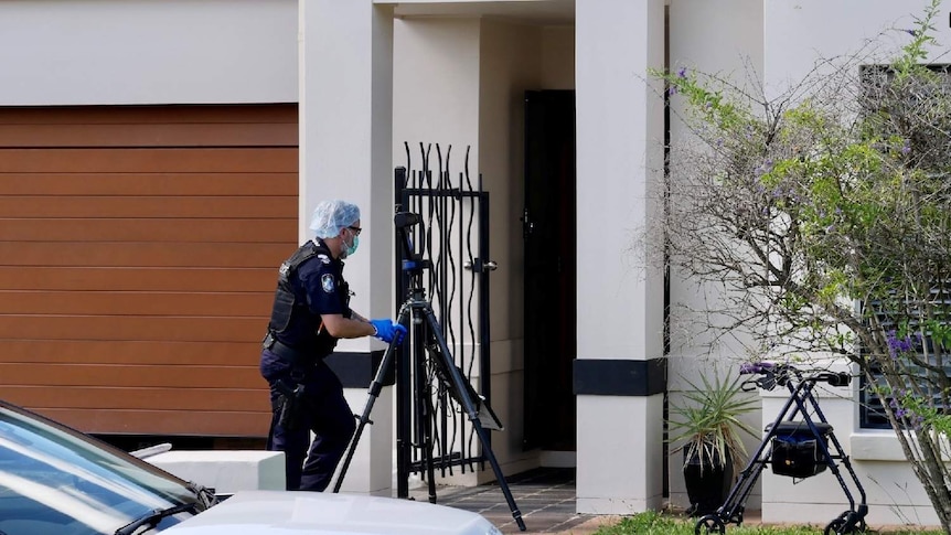 A police officer in gloves and cap takes photos at the entrance of the house.
