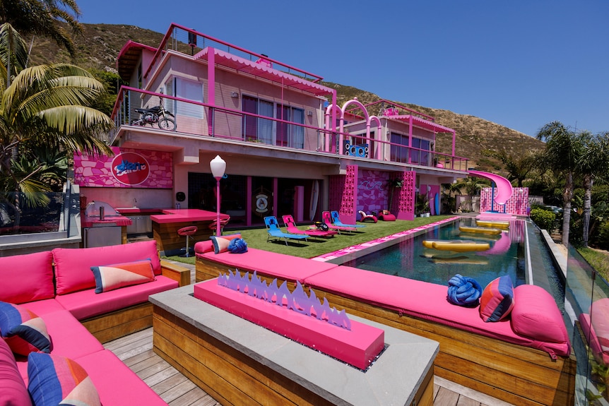 A wide shot of a two story house complete with a hot pink slide, hot pink lounge chairs and a fake fire.