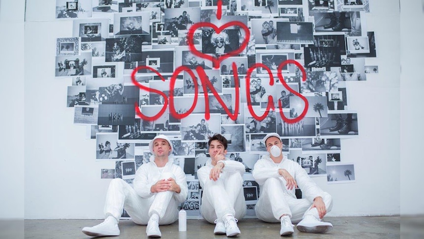 A 2018 press shot of Thundamentals sitting in front of a wall of photos with spraypaint reading 'I Love Songs'